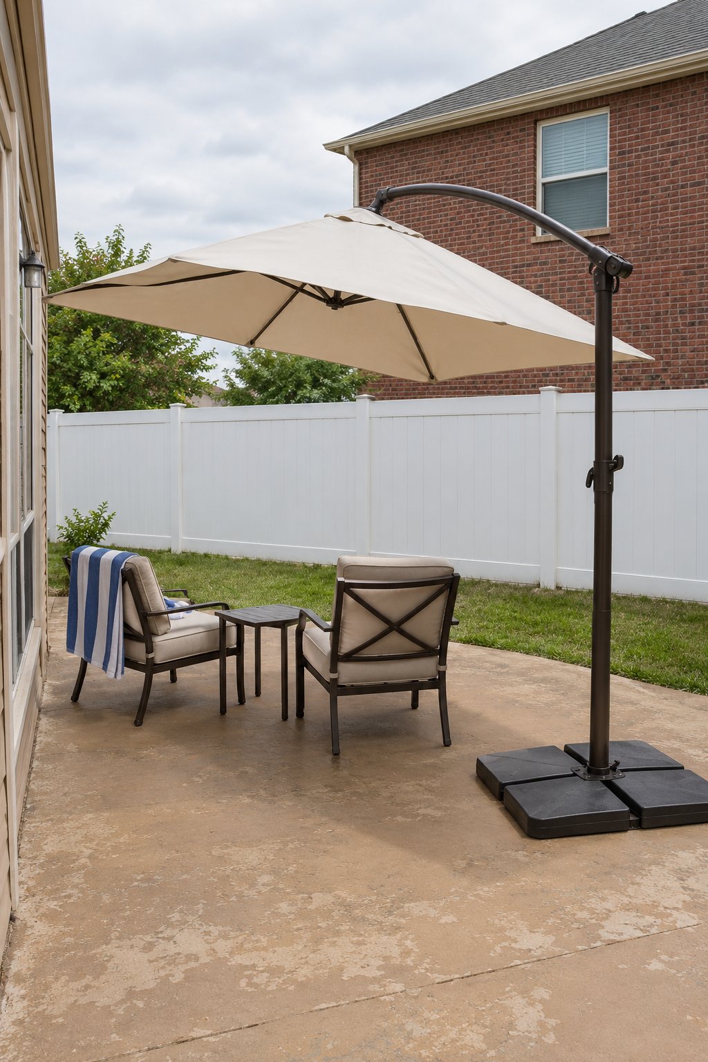 Patio privacy ideas for an overlooked yard, an offset cantilever umbrella tilted toward the neighbor's two-story house, shading and hiding two chairs on a concrete patio