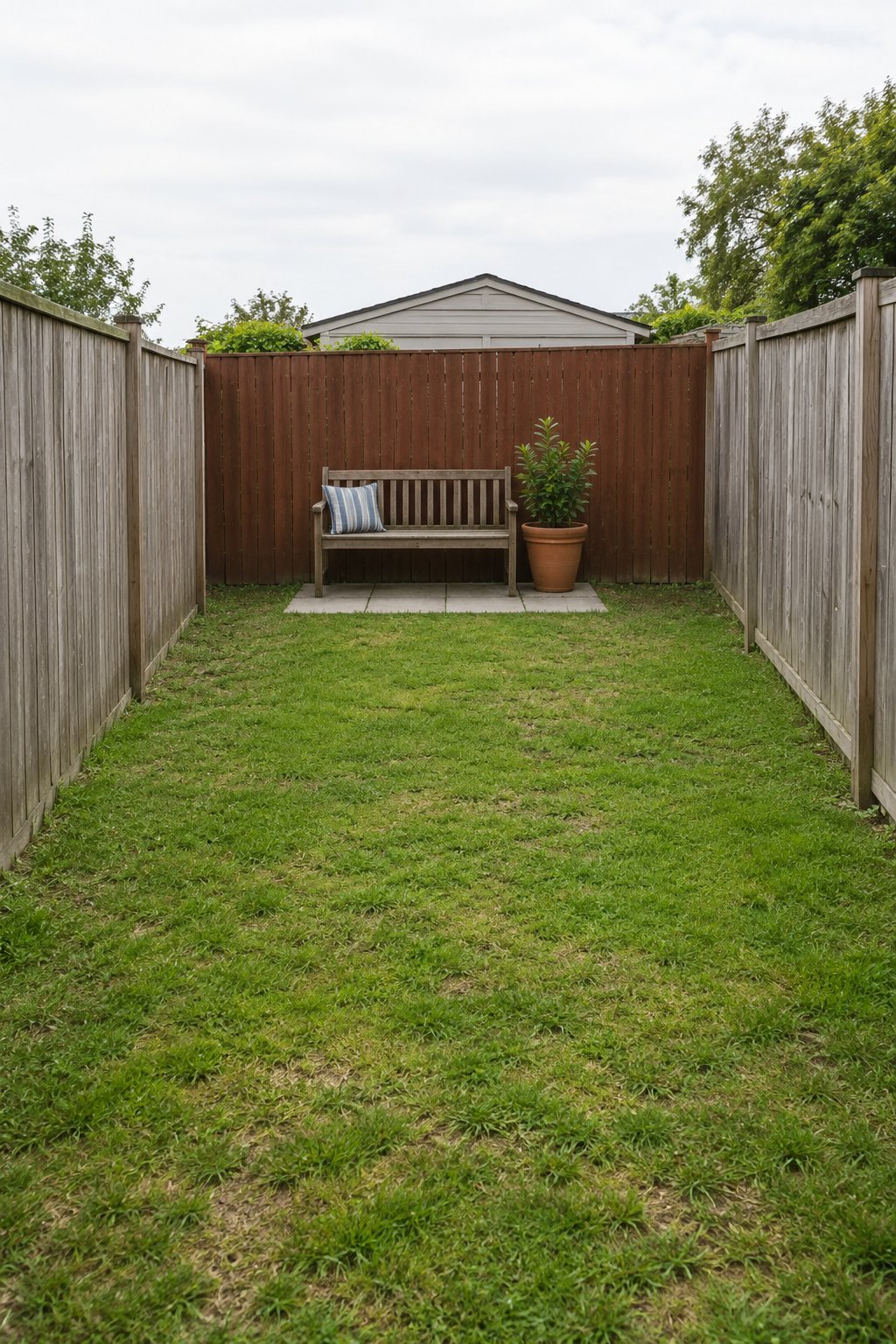 Backyard ideas for small yards, a wooden bench on a small paver pad against the back fence with one large pot beside it at the end of a narrow lawn